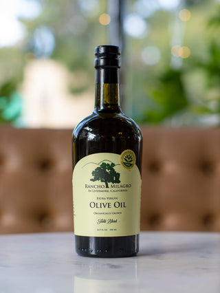 A bottle of Rancho Milagro extra virgin olive oil on a marble surface with a blurred background.