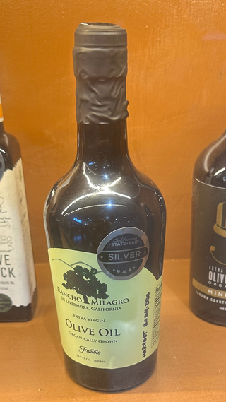 Bottle of Rancho Milagro Frantoio olive oil with a California State Fair Silver award badge in a display case.