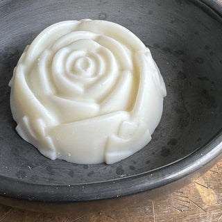 Large round soap, relief molded like a rose blossom, but flat on the lower surface, resting on a black ceramic dish.