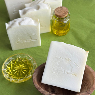 Bar of olive oil in a wooden dish. Behind are a cut-glass saucer of oil, 4 or more additional bars and a small corked container of oil.