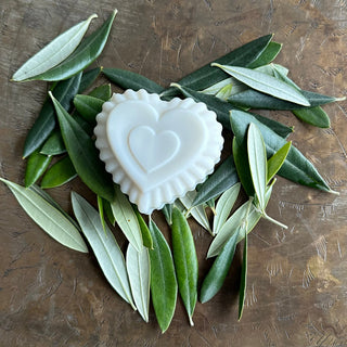 A large heart-shaped soap, with three tiers of texture, resting on a bed of olive leaves