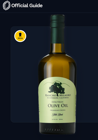 A 500ml (older) bottle of Rancho Milagro Extra Virgin Olive Oil centered on a dark navy background, with an 'Official Guide' banner for the New York International Olive Oil Competition at the top and a gold 2026 award badge on the left.